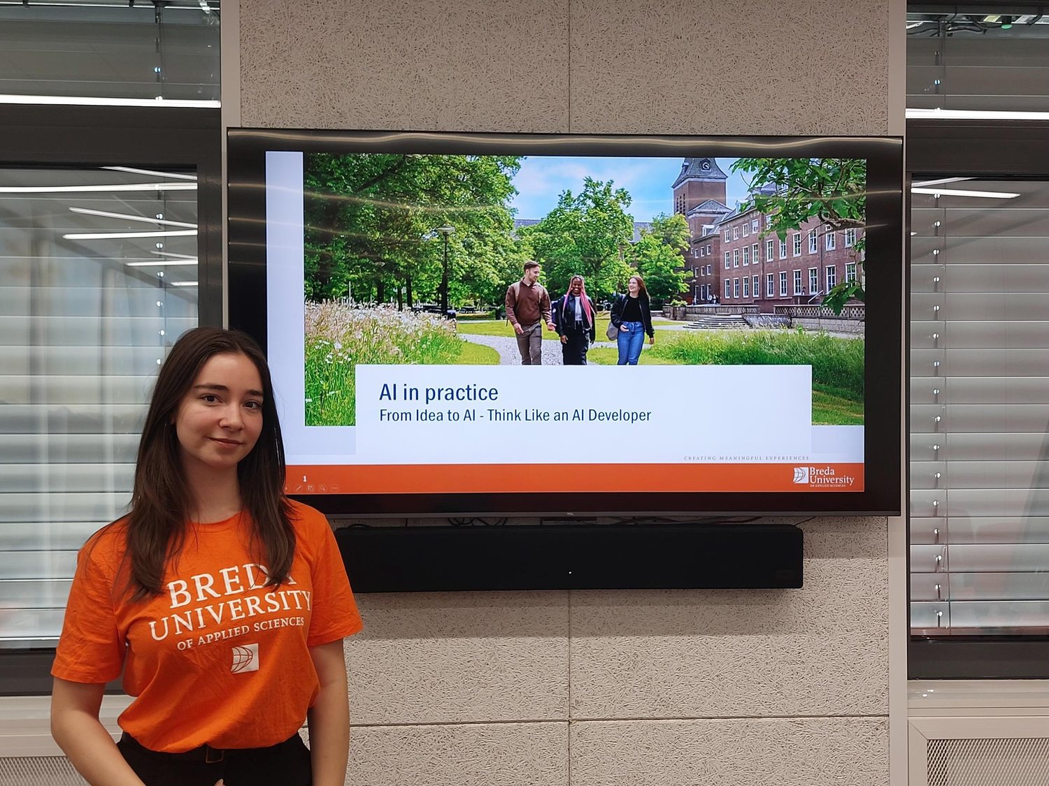 A student beside a screen showing the title slide AI in practice